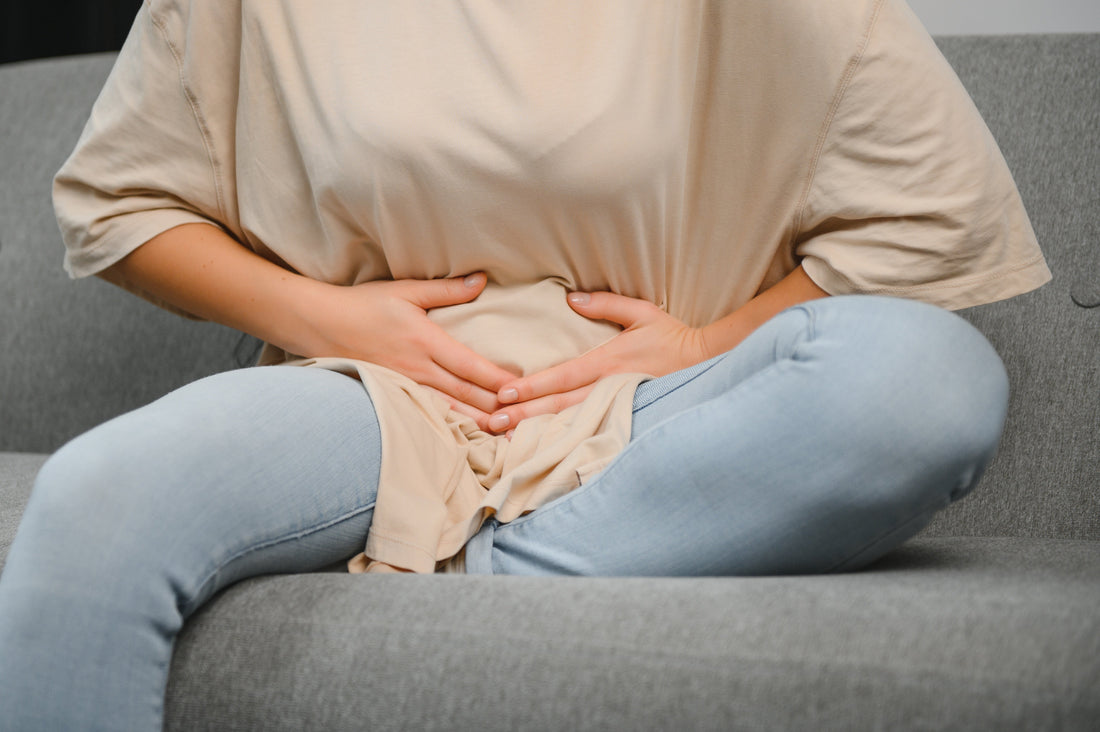 Woman holding her lower abdomen sitting on couch illustrating how to regulate menstrual cycle with PCOS naturally